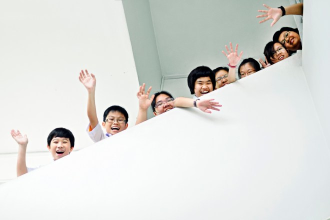 Young children waving behind a staircase