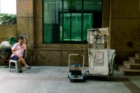Man smoking while sitting on one side, with a pushcart of hardware equipment on the other side of the photo (Photo by Ng Shi Wen)
